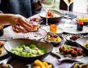 woman hand eating food in restaurant. wine, cheese, meat, vegetables and other appetizers on table